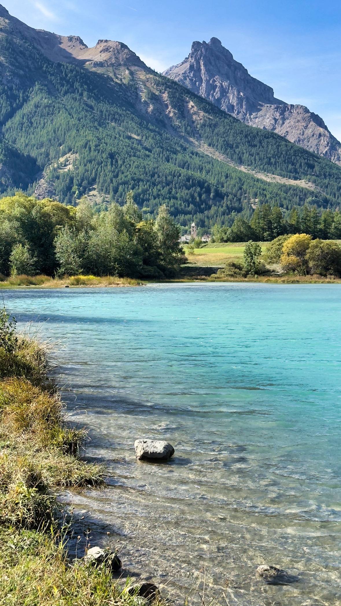 A turquoise glacial river beside Le Monêtier-les-Bains, with a church spire and a pointed peak in the background