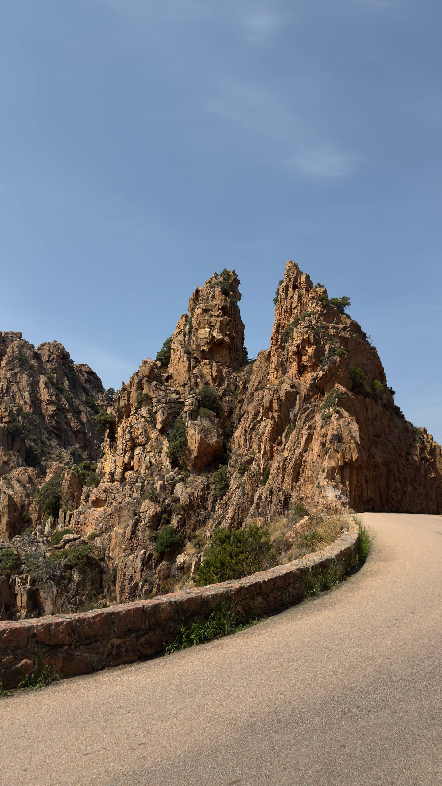 Wind-eroded red granite pinnacles of the Calanques de Piana with a road curving below