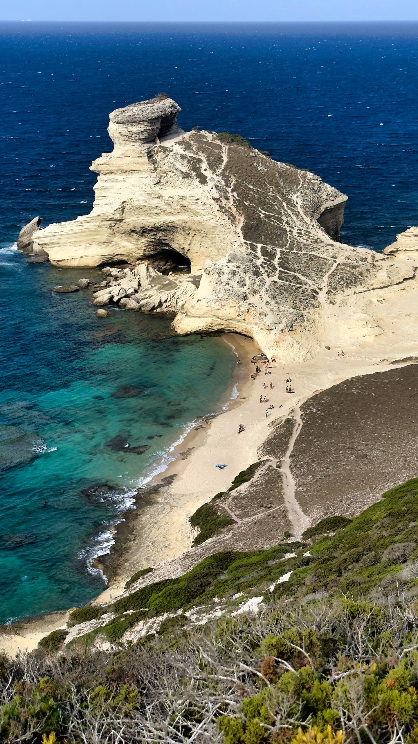 A small crescent of sand at the base of a white limestone cliff