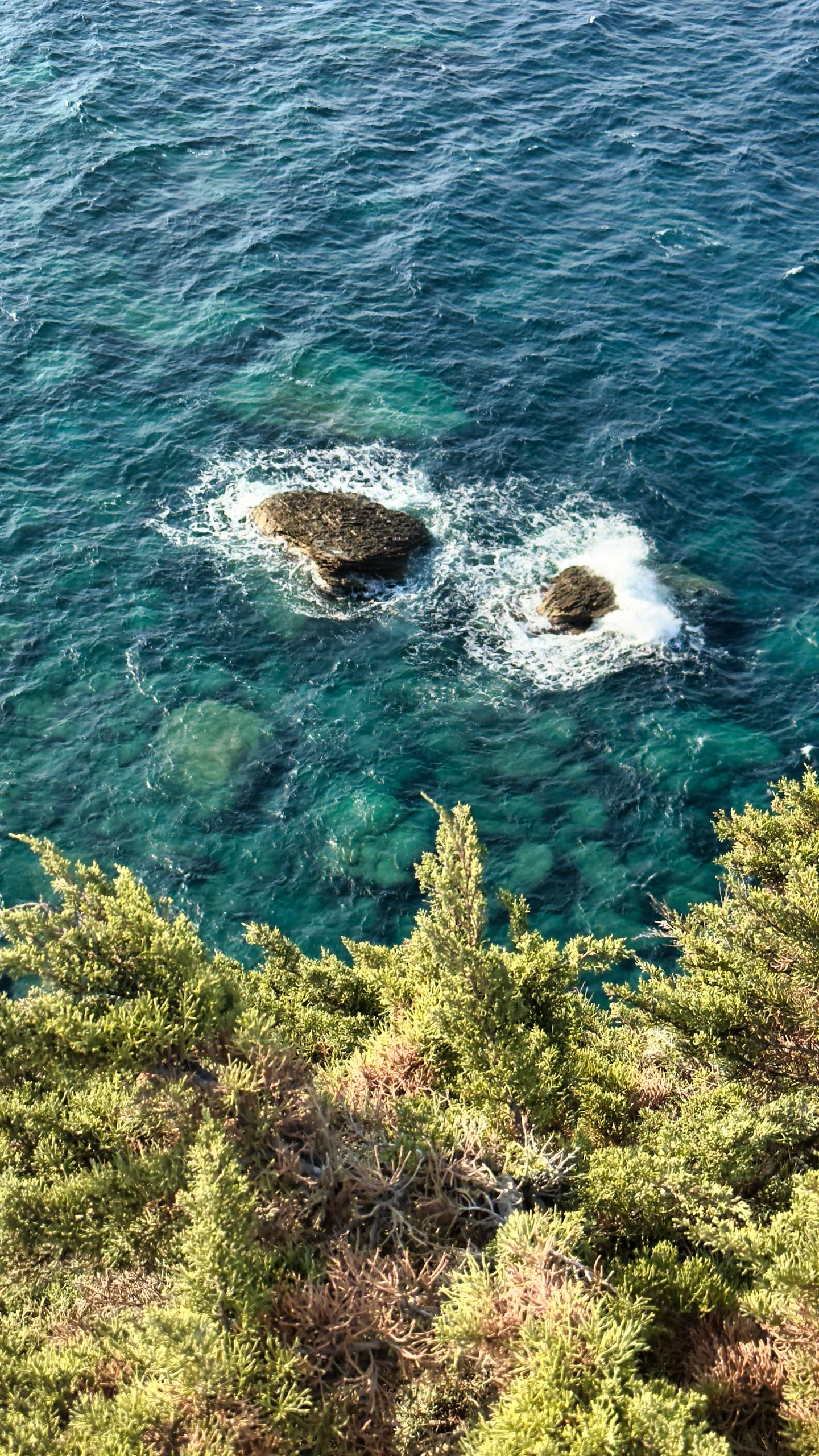 Two rocky outcrops in turquoise water seen from a clifftop
