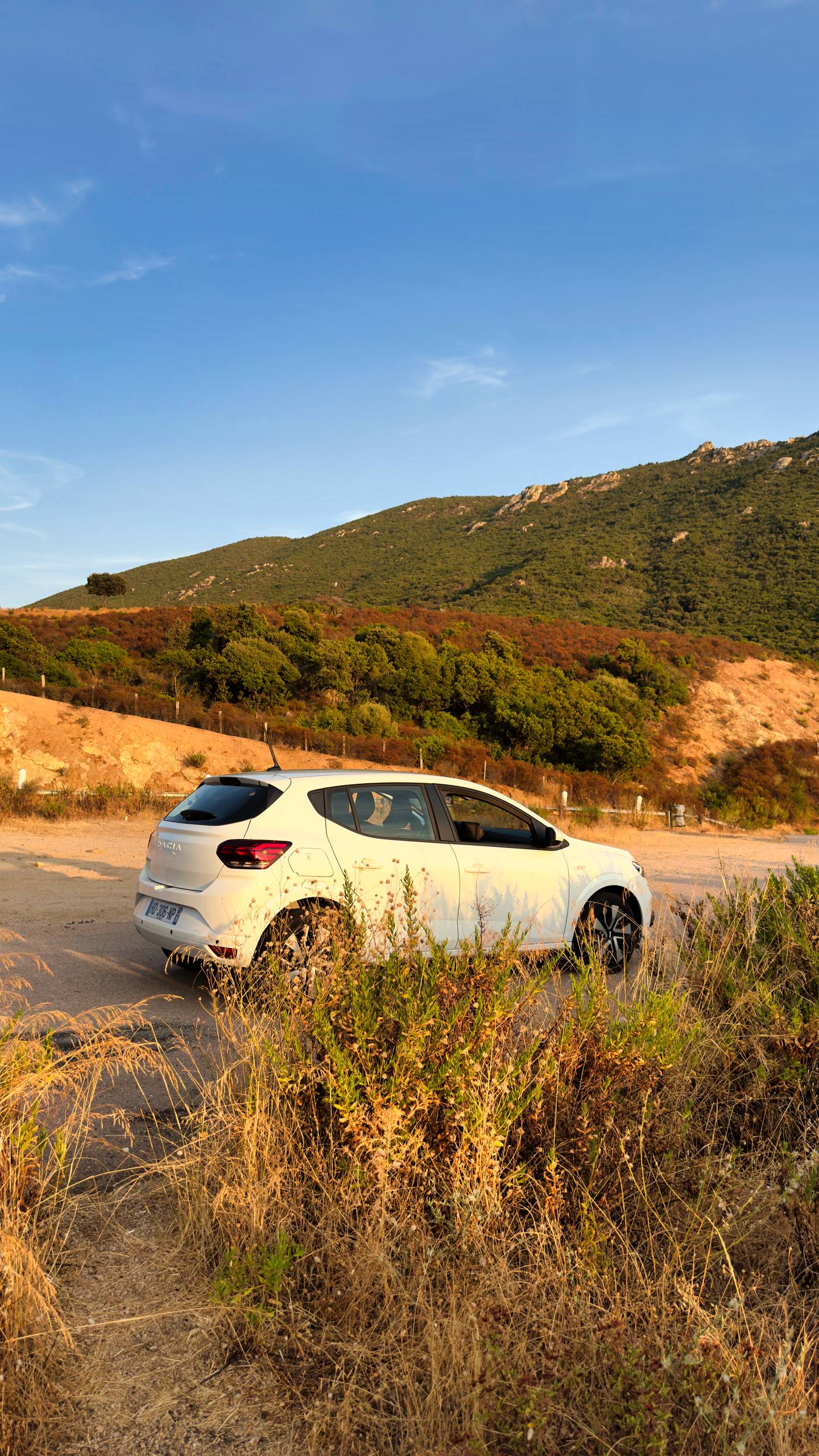 A white Dacia Sandero parked on a dirt pullout in golden hour light