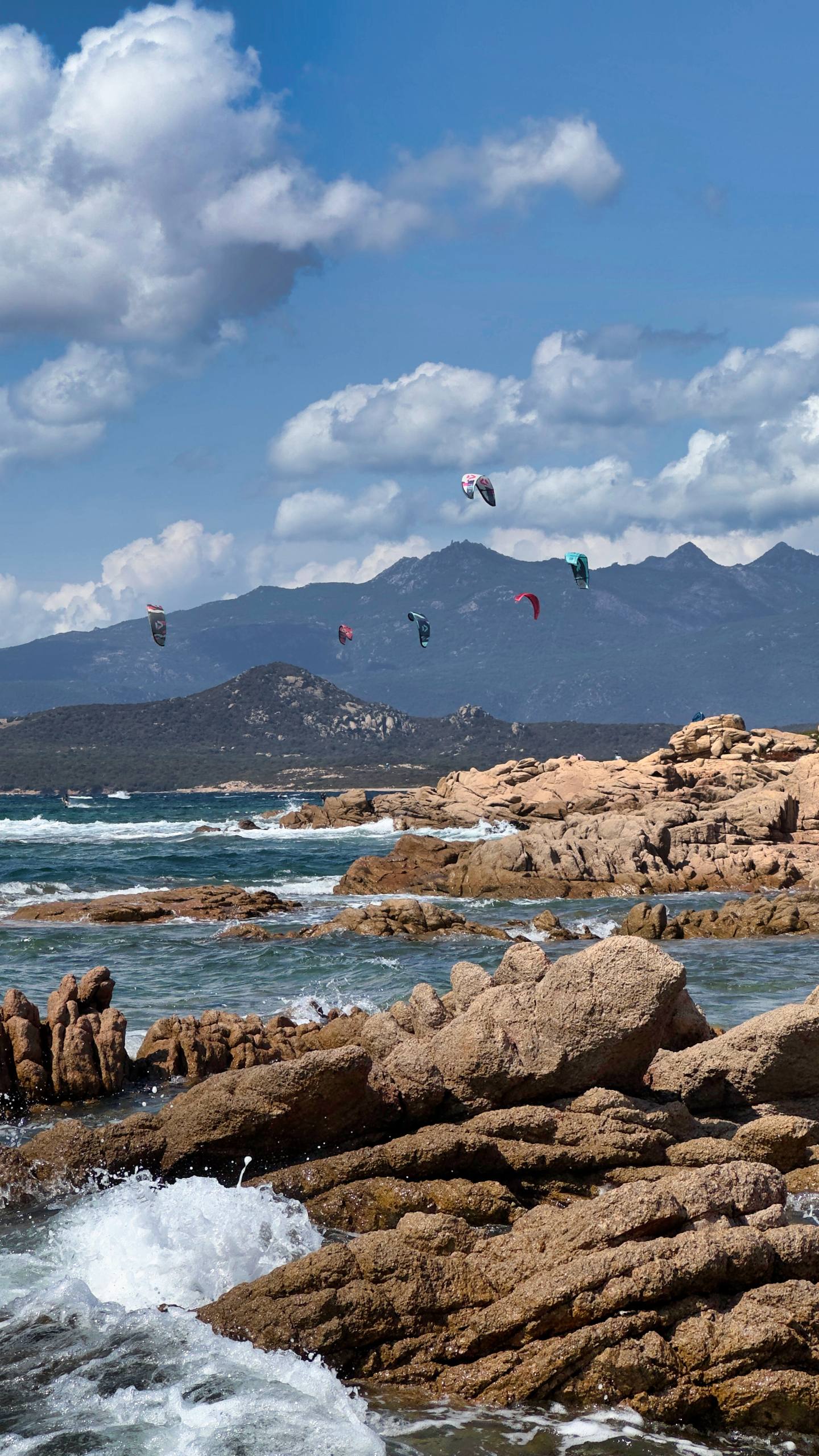 Kitesurfing kites flying over the sea with pink granite mountains behind