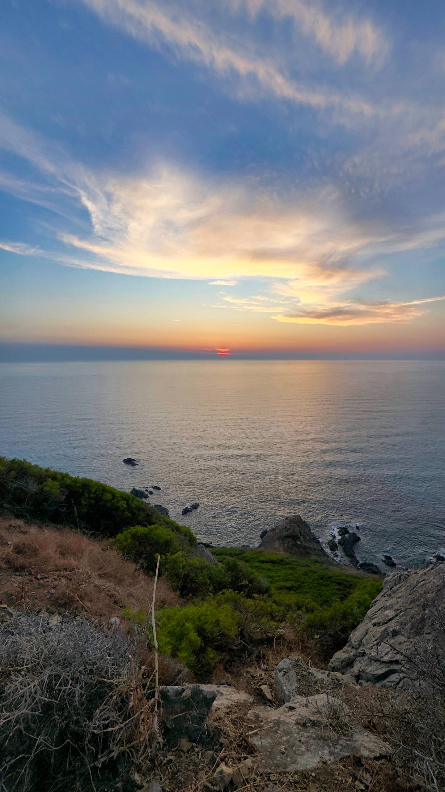 A red sun touching the Mediterranean horizon with cirrus clouds catching the light