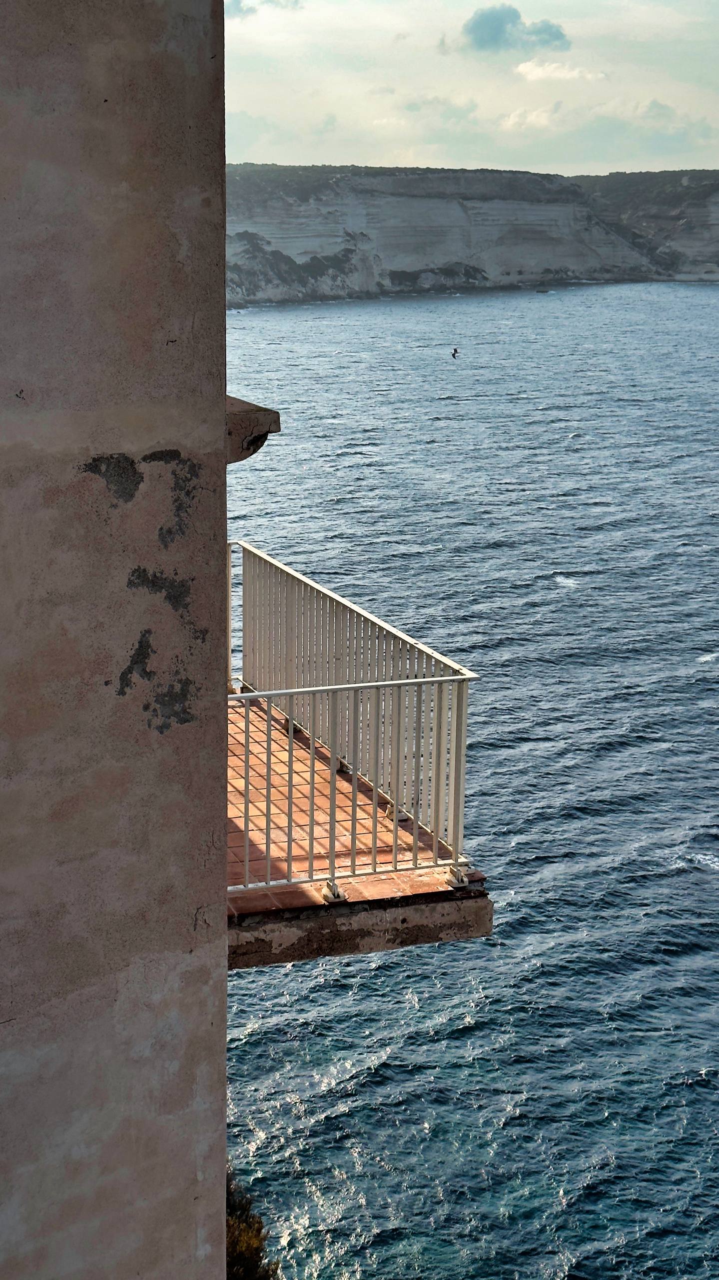 View from inside a stone tower onto a small balcony with the Bonifacio cliffs in the distance