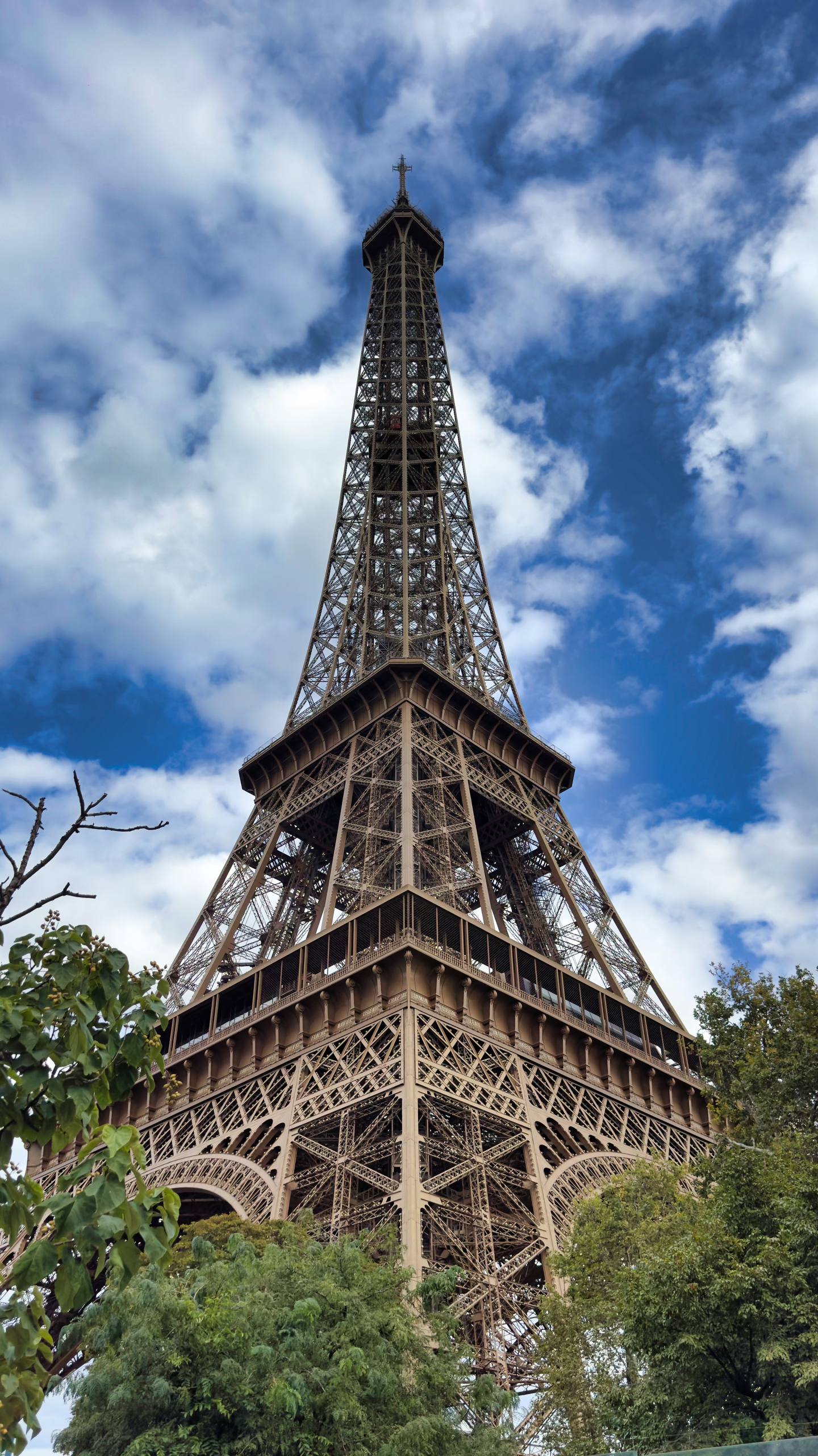 The Eiffel Tower seen from below against a blue sky with scattered clouds