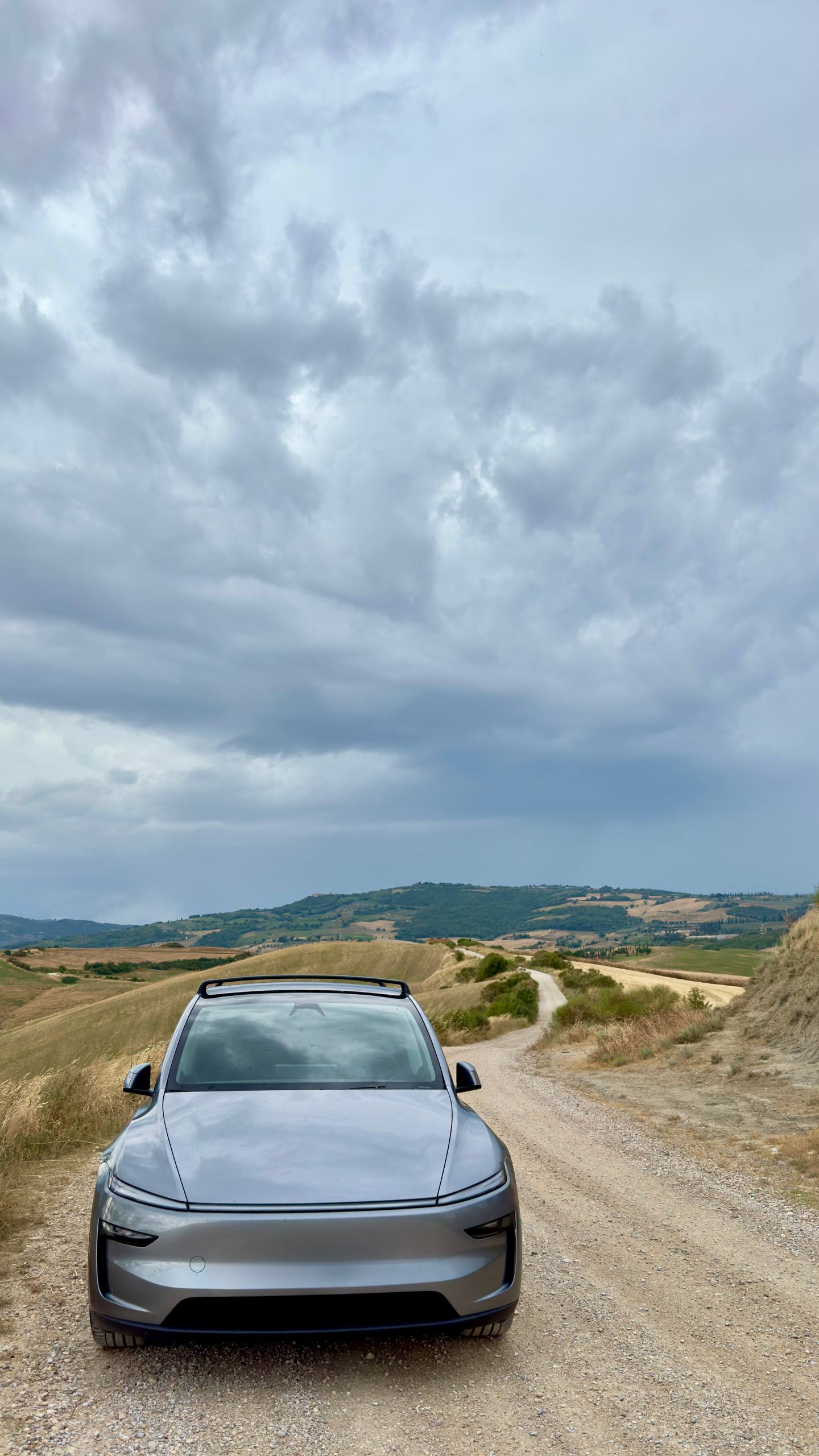 A car parked on a dirt road winding through the rolling golden hills of the Crete Senesi