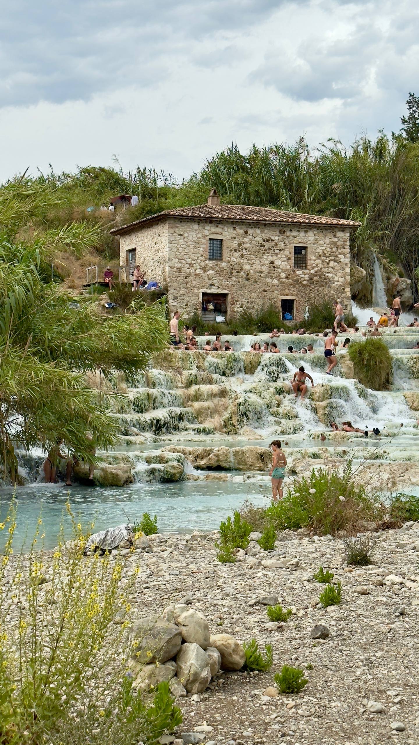 The Cascate del Mulino thermal waterfalls at Saturnia, with bathers in milky turquoise travertine pools beside an old stone mill
