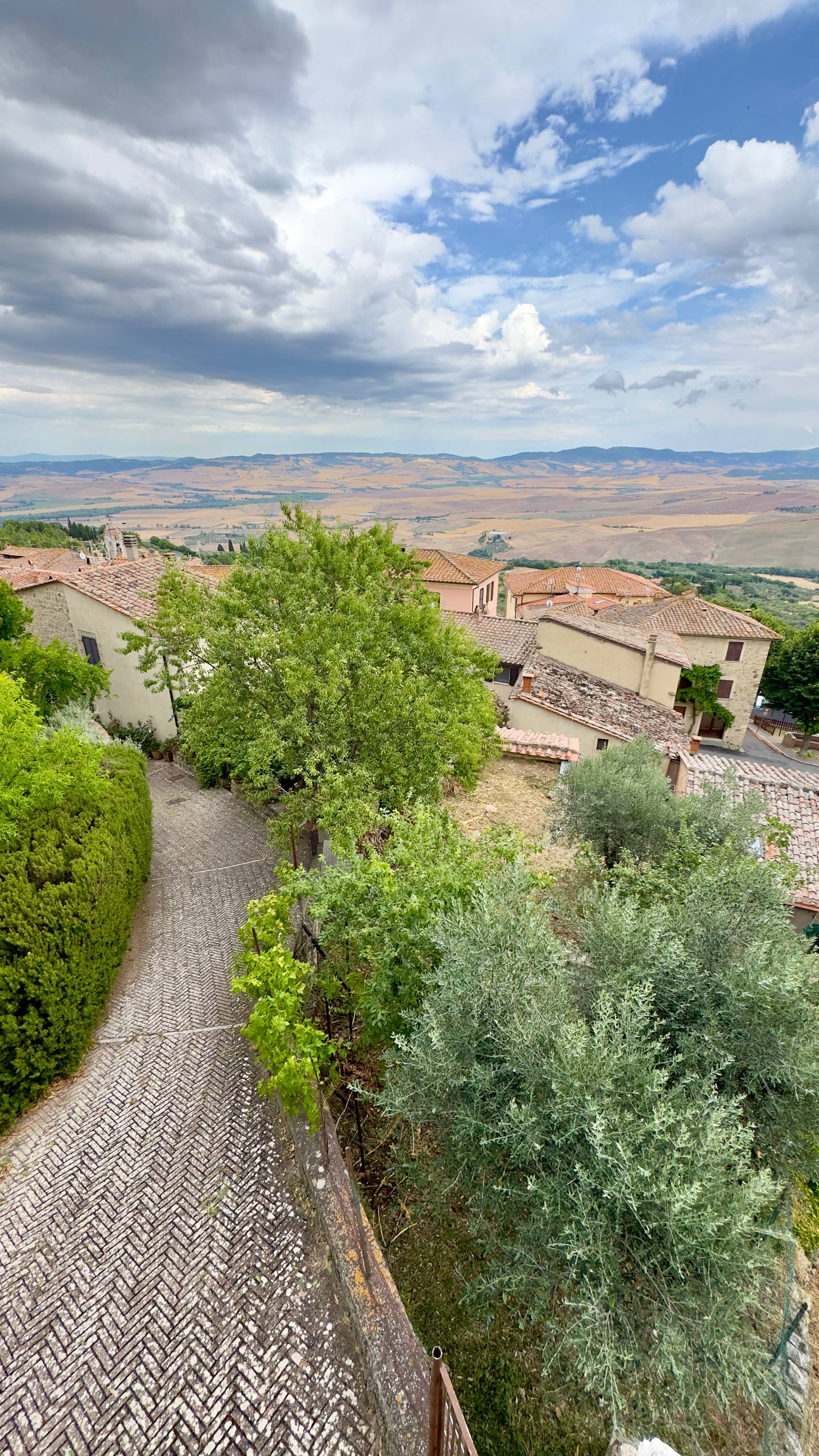 View over terracotta rooftops of a Tuscan hilltop town across the Val d'Orcia toward distant hazy mountains